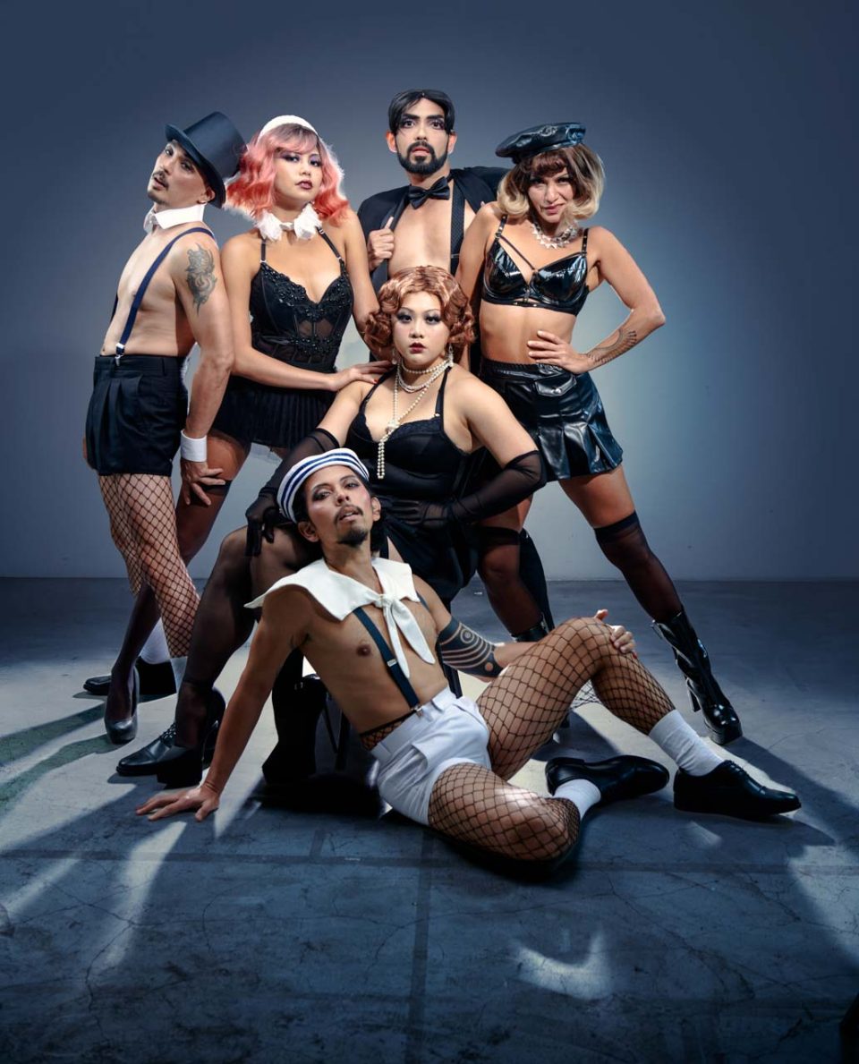Singapore advertising portrait photography: publicity portrait. The Cabaret ensemble in black cabaret costumes, fishnets and bowler hats posed on the studio floor, one performer reclining in front, for Sing'Theatre's Cabaret