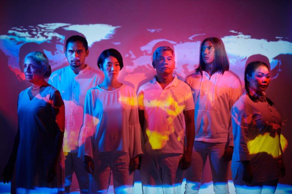 Singapore advertising portrait photography: theatre key art. Six performers of The Year of No Return in magenta and yellow light under a projected world map, group portrait for The Necessary Stage's key visual