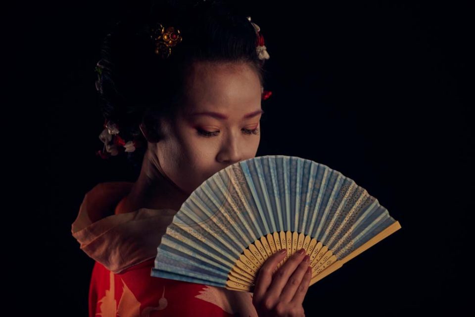Singapore advertising portrait photography: theatre key art. A performer with ornaments in her hair holding a paper fan over her face, eyes lowered, production visual for The Theatre Practice's 四马路