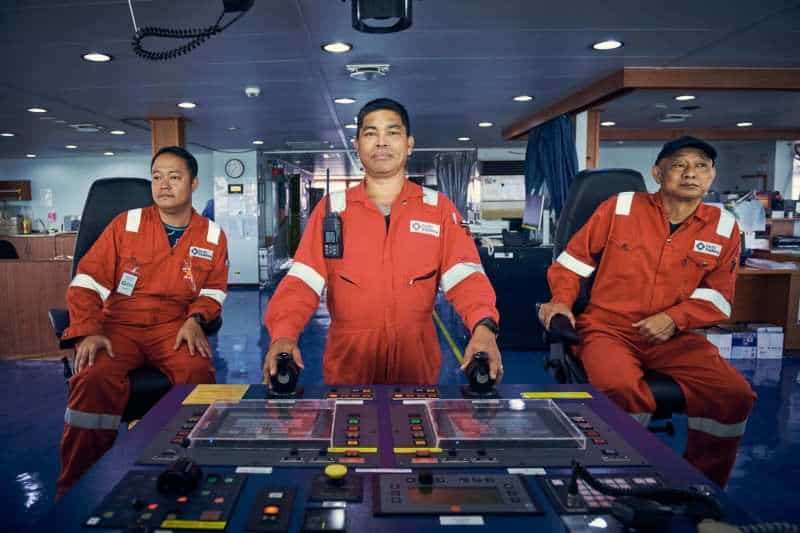 Singapore industrial videography: Three offshore crew in orange coveralls at the bridge console of the Safeen Centurion 2 — Singapore industrial photography, offshore crew portraits