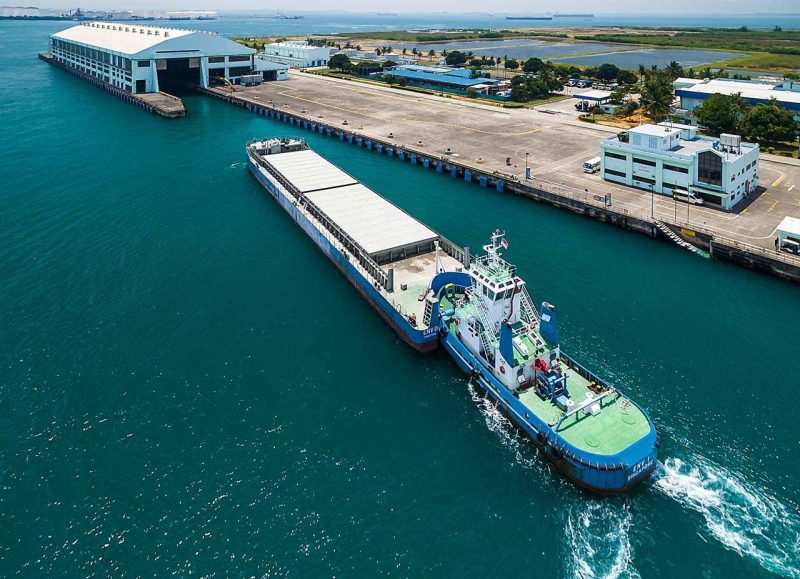 Aerial view of a tugboat pushing a covered waste transfer barge alongside the terminal — industrial photography Singapore, waste management, aerial maritime photography