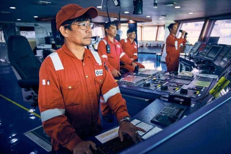 Crew in orange coveralls and hard hats operating the bridge controls of an offshore support vessel — Singapore industrial photographer, men at work