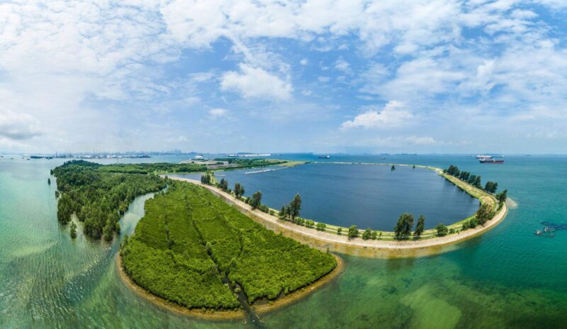 Containment bund and lagoon at Semakau Landfill from the air, mangroves in the foreground, ships on the horizon. Singapore industrial photographer.