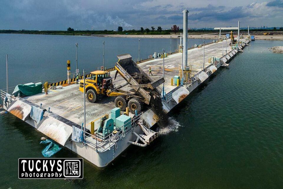 Dump truck spreading incineration ash into a new landfill cell at Semakau, barged in from the Tuas Marine Transfer Station — aerial drone photography, Singapore