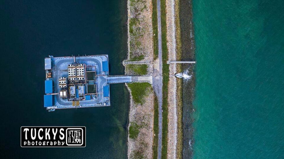 The Semakau containment bund from directly above, the line between sea and lagoon with the jetty structure at its centre — drone photography Singapore