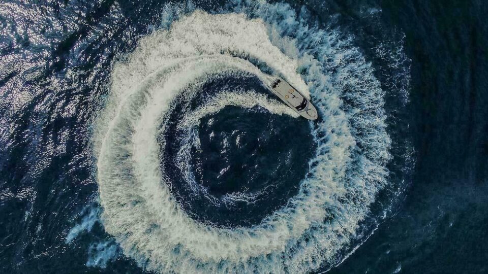 Fast interceptor pulled through a full-circle manoeuvrability test, its wake closing the loop, from directly above — drone photography of a sea trial