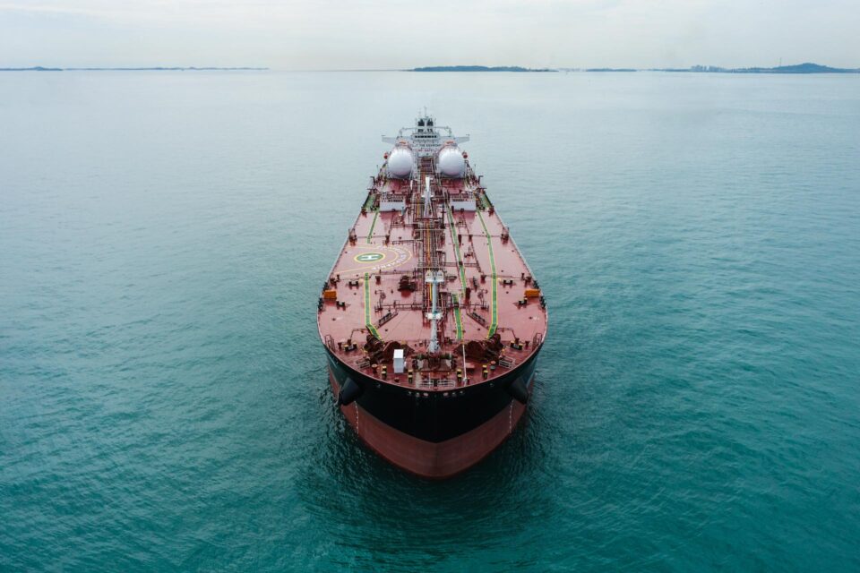 Tanker Proteus Stephanie seen head-on from the air at Singapore's Eastern Petroleum Anchorage, bow toward the camera, red deck running back to twin white tanks — drone photography Singapore