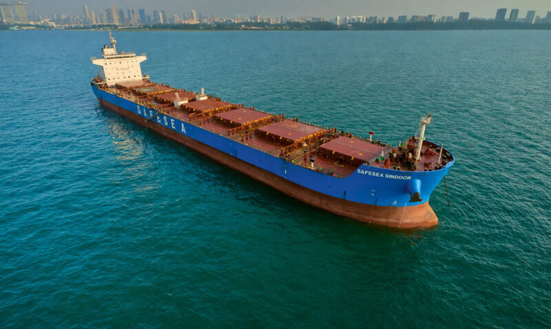 Cargo ship aerial view: bulk carrier Safesea Sindoor at anchor in Singapore waters, Marina Bay skyline on the horizon — drone photography Singapore