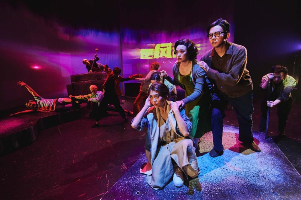 Singapore theatre photography: stage photography. Under magenta light a woman kneels clutching her head as a man grips her shoulders, performers sprawled on the stage behind, in All The World's A Sea
