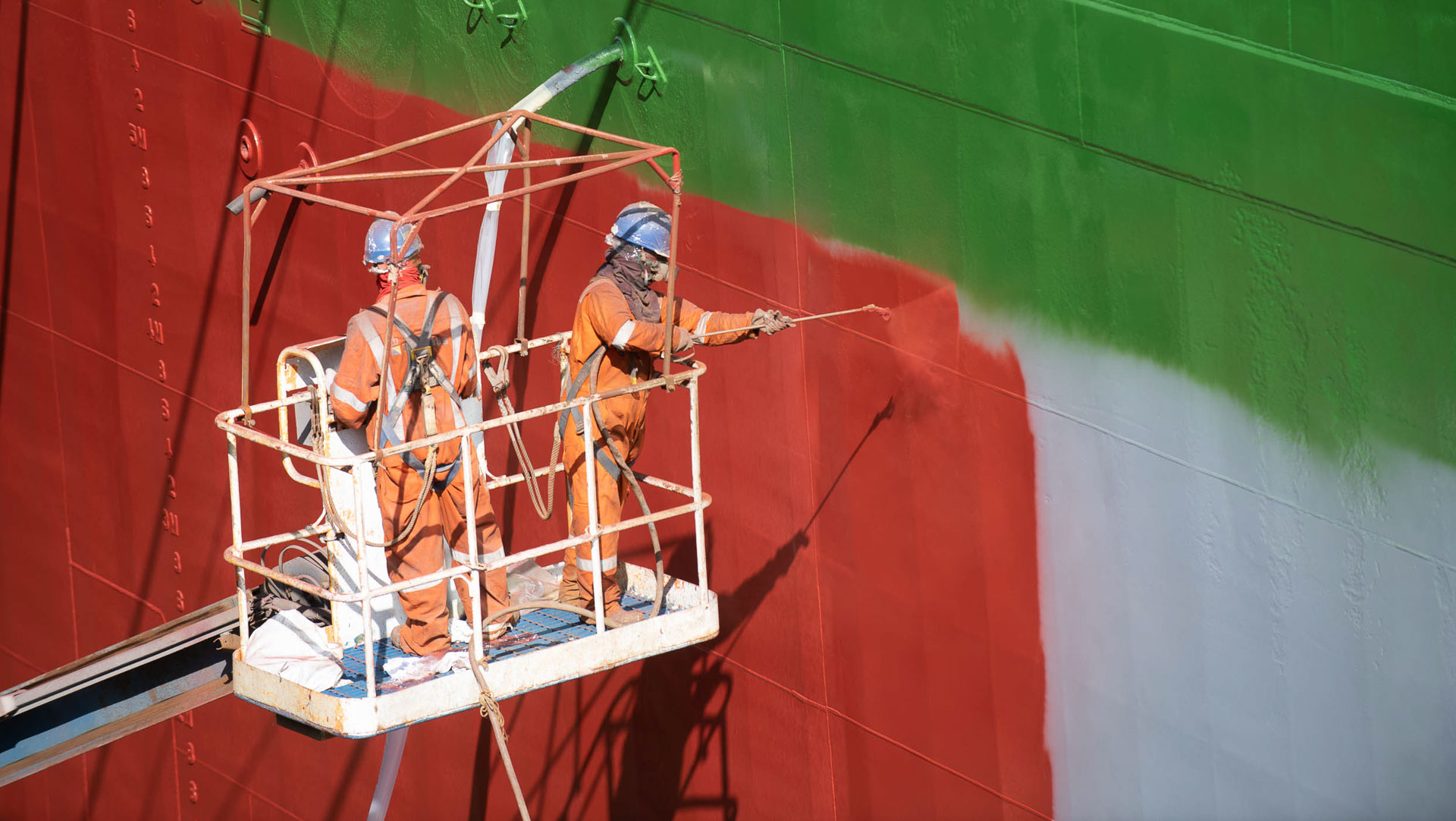 Two painters in a lift basket spraying the hull of the JP88 Stork at Keppel Shipyard, Singapore shipyard photography