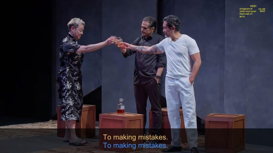Singapore theatre photography: theatre video still. Video still from The Commission: three performers raise their glasses in a toast, subtitled To making mistakes