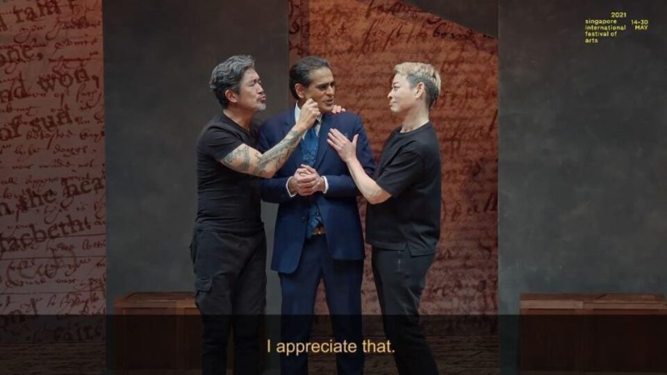Singapore theatre photography: theatre video still. Video still from The Commission: two performers embrace a third, in a suit, between them, subtitled I appreciate that