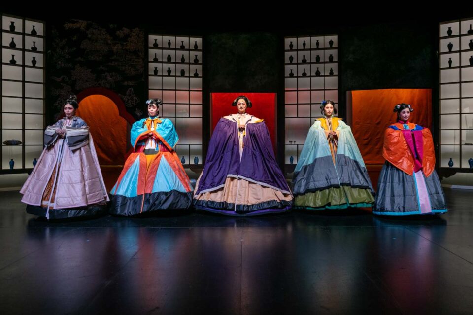 Singapore theatre photography: production photography. Five performers in voluminous Qing-style costumes stand in a line before lattice screens and red panels, in The Crab Flower Club