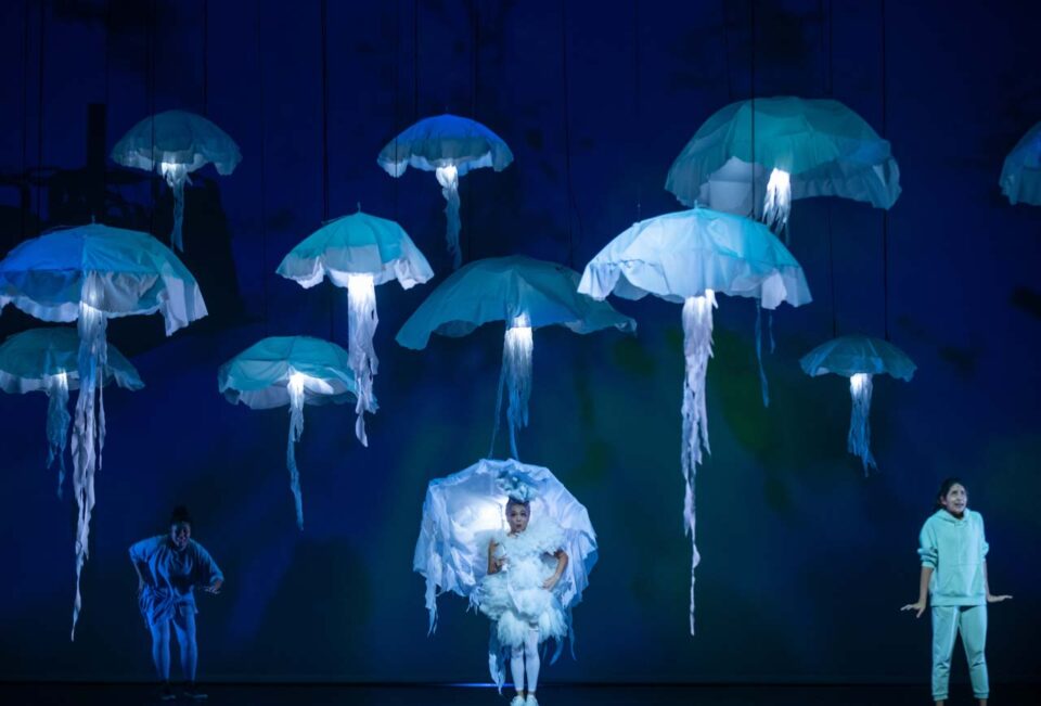 Singapore creative portrait photography: underwater portrait. Glowing jellyfish float above the stage as a performer in a white jellyfish costume stands between two others, in The Feelings Farm